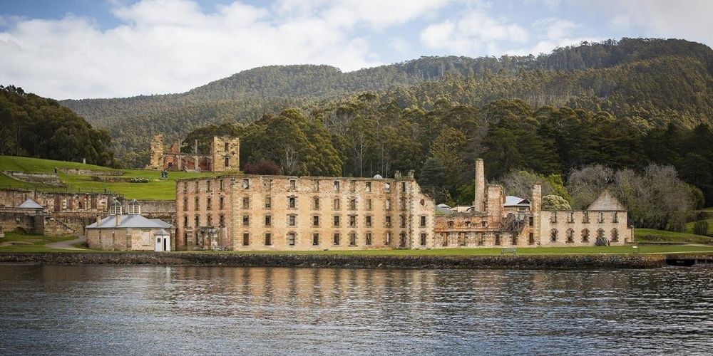 Port Arthur Historic Site beside calm waters, with historic stone buildings set against a forested mountain landscape